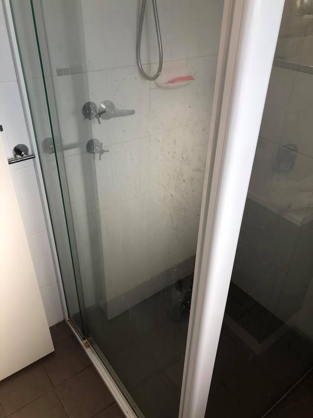 Shower glass clouded with soap scum and mineral marks before cleaning