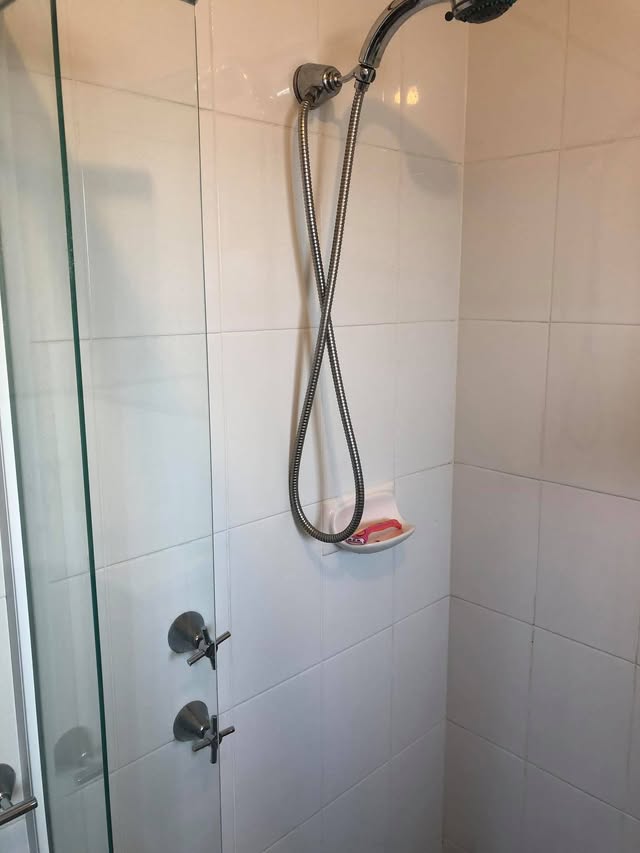 Polished shower head, hose and tapware against clean white tiles