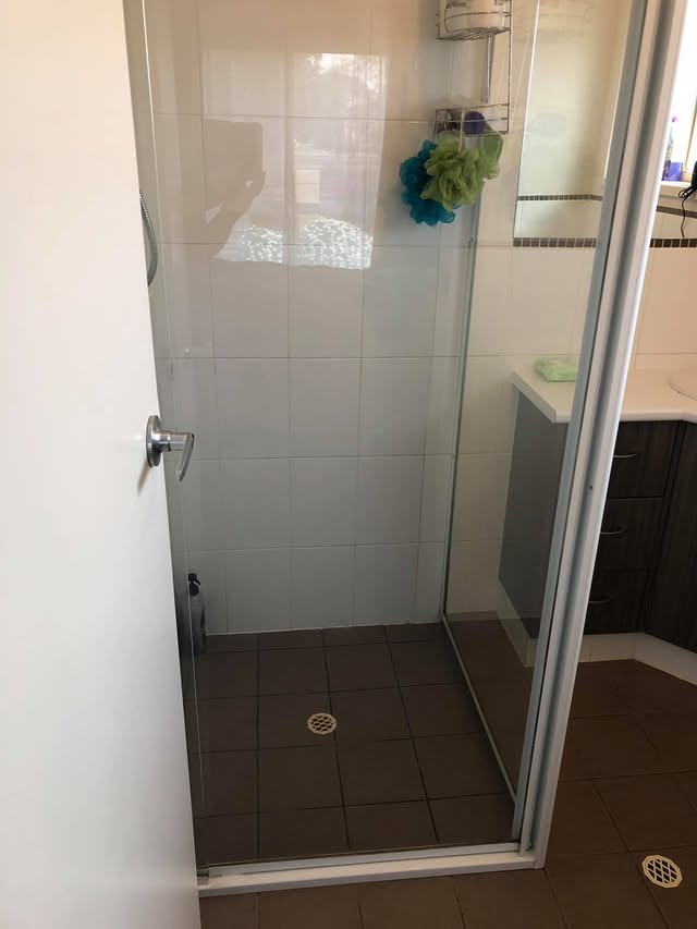 A restored shower with its glass door open — spotless tiles, screen and floor