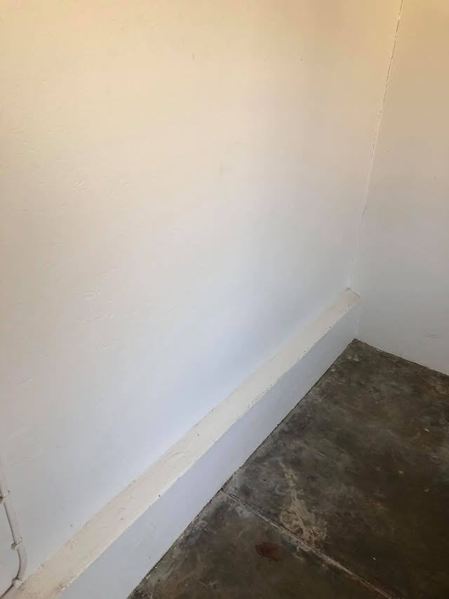 The same wall and skirting board washed clean, floor swept